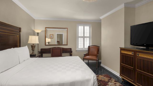 A wide view of a hotel room with a bed, TV, desk, chair, and mirror.