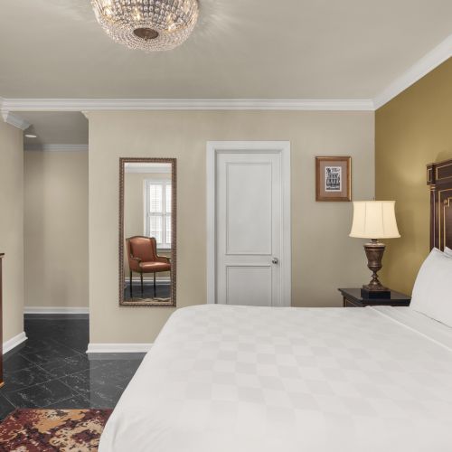 A cozy bedroom with a large bed, TV on a wooden cabinet, a mirror, a lamp on a nightstand, and stylish decor, including a rug.