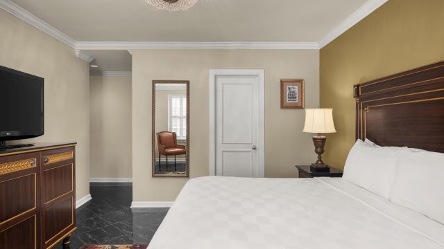 A hotel room with a large bed, TV, mirror, and lamp.