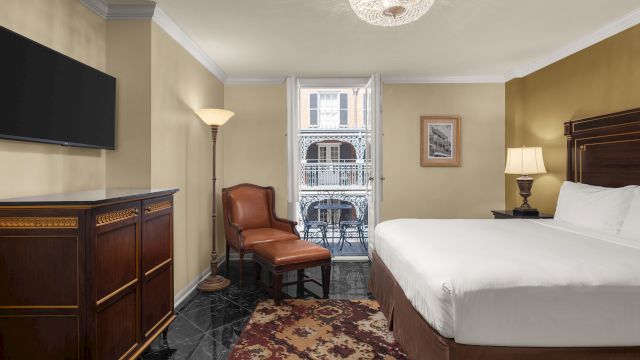 A hotel room with a bed, TV, chair, and balcony