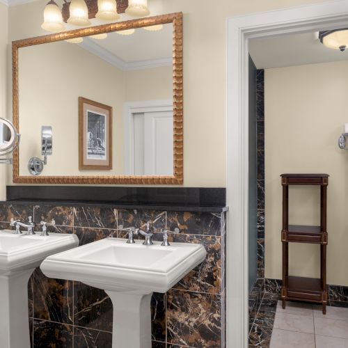 Bright bathroom with dual sinks, large mirror, towel rack, and a small shelf next to the toilet.