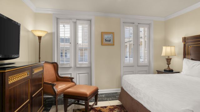 A hotel room with a bed, chair, TV, and lamp.