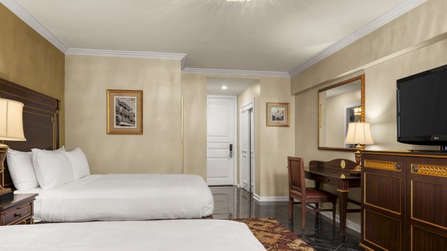 A hotel room with two beds, a desk, and a TV on a dresser.