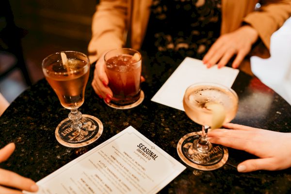 Three people are at a table with cocktails and a menu on a dark surface.