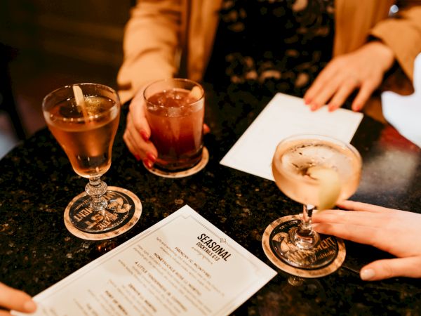 Three people are at a table with cocktails and a menu on a dark surface.