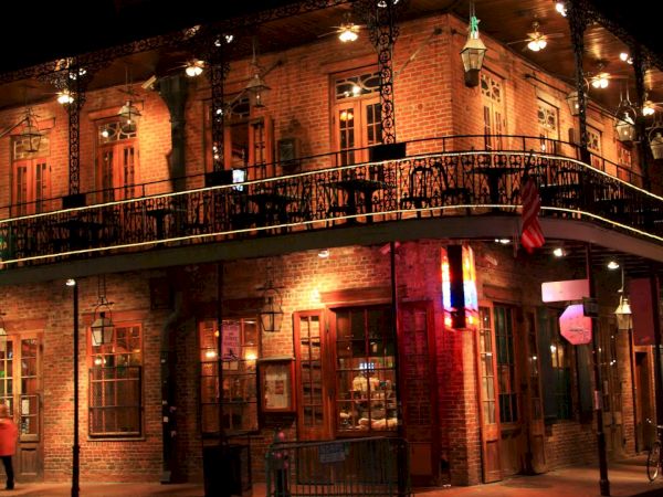 A brick, two-story corner building with a balcony, warm streetlights, and hanging lanterns, giving a cozy, historic feel.