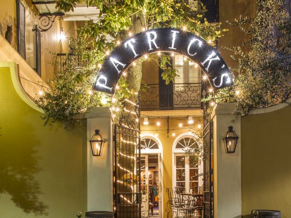 A warmly lit entrance to a place named Patrick's, with patio chairs and tables visible beyond decorative iron gates.