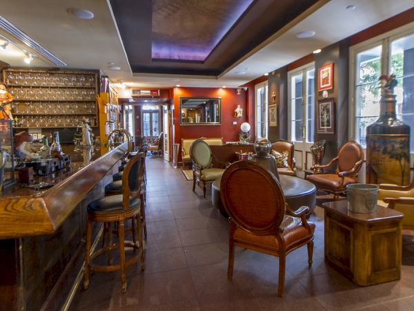 The image shows a cozy bar interior with a long counter, bar stools, and elegant seating. The walls are adorned with art and decor.