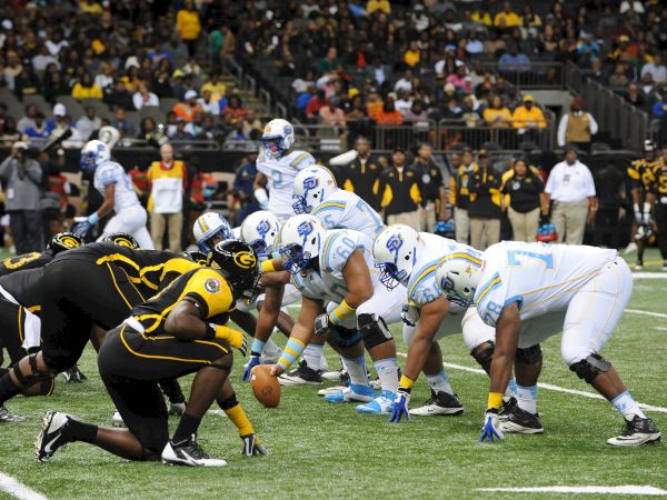 A crowd of players in blue and black pile up during a football game, with a ball on the turf near the line.