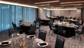 The image shows an elegantly set dining room with round tables, chairs, and tableware, suitable for a formal event or banquet.