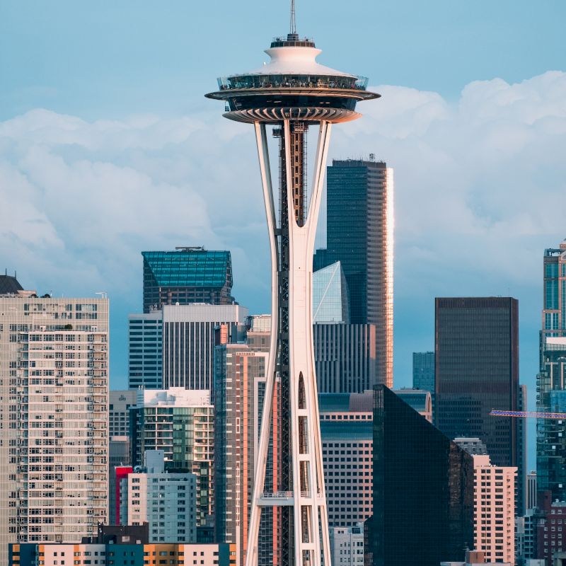 The image shows the Space Needle with a backdrop of skyscrapers and clouds in a cityscape.