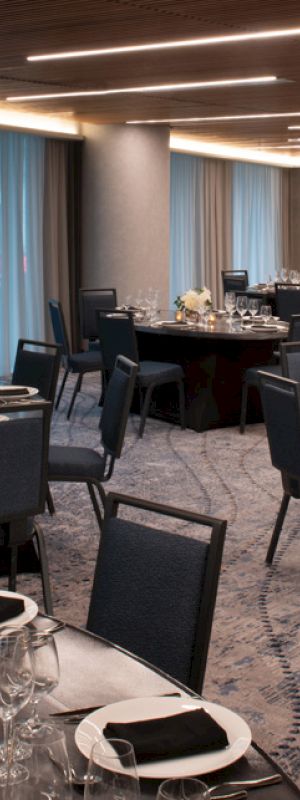 The image shows an elegantly set dining room with round tables, chairs, and formal table settings, including glassware and floral centerpieces.